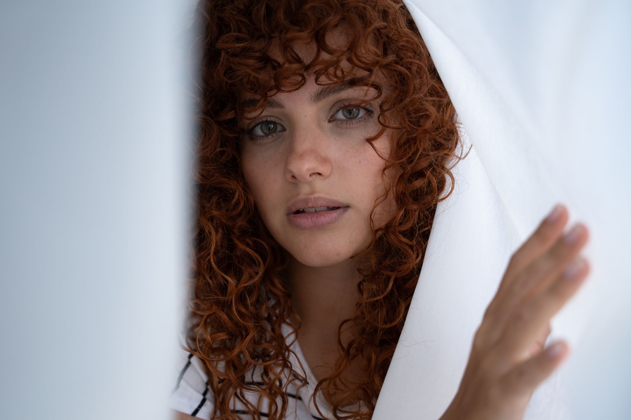 Woman with curly red hair behind white fabric.