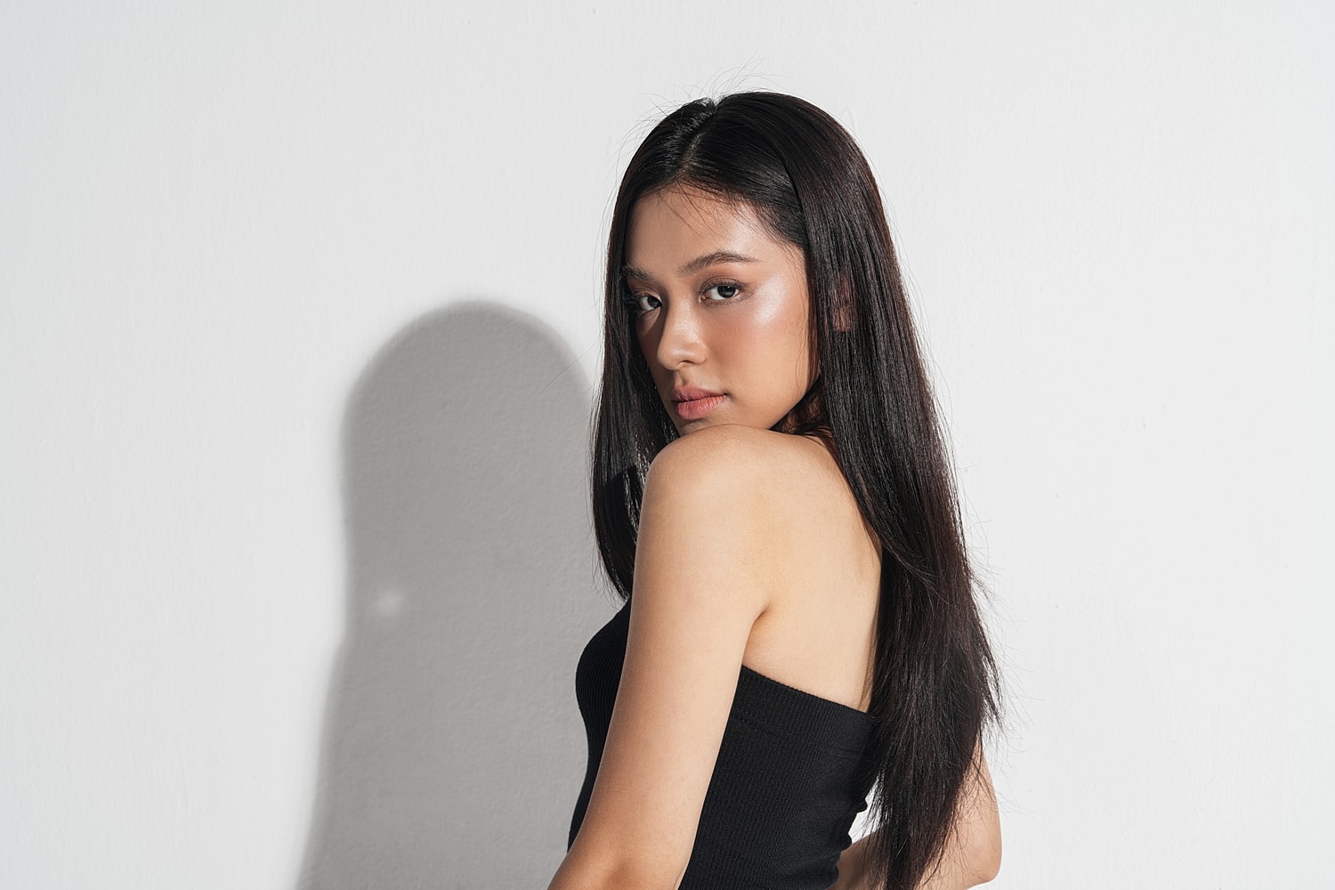 Young woman with long hair against white wall.